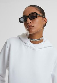 Felpa bianca con cappuccio, occhiali neri angolari, collana choker in argento. Texture liscia, design moderno, accenti e colori minimal.