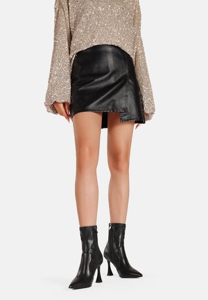Stivaletti neri in pelle con punta affusolata e tacco a blocco, abbinati a una mini gonna nera in pelle e a una maglietta oversize beige glitterata.