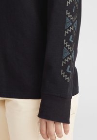 Black long-sleeve shirt featuring geometric patterns in teal and gray on the sleeve, with ribbed cuffs and soft cotton material.