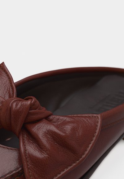 Κοντινή λήψη ενός καφέ δερμάτινου γυναικείου παπουτσιού, με μεγάλο δεμένο φιόγκο στην περιοχή των δαχτύλων, σε απλό φόντο.