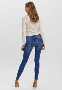 Jeans ajustados en denim de color azul oscuro, con una cintura de altura media, diseño de cinco bolsillos y un ligero efecto de desvanecimiento. Combinados con una blusa ceñida de color crema y tacones.