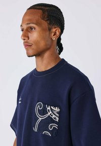 Marineblauwe t-shirt met korte mouwen, voorzien van een tekstuur pocket met een draaiend wit patroon. Stiksels langs de hals en mouwen.