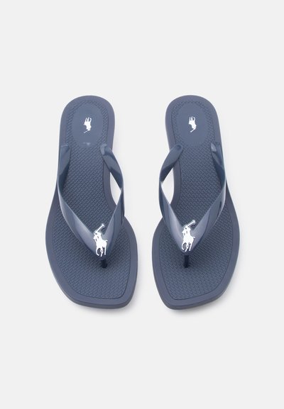 Ζευγάρι σκούρων μπλε σαγιονάρες με υφή στη σόλα και λευκά λογότυπα παίκτη πόλο στα λουράκια, φαίνεται από πάνω πάνω σε ανοιχτό φόντο.