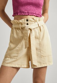 Pantalones cortos de algodón amarillos con cintura alta, presillas para cinturón y un cinturón de tela atado. Presenta dos bolsillos frontales y un corte relajado.