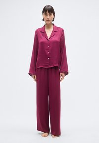 Ensemble de pyjama bordeaux en satin léger, comprenant un haut boutonné à col et un pantalon amples, avec des manches longues et une silhouette décontractée.
