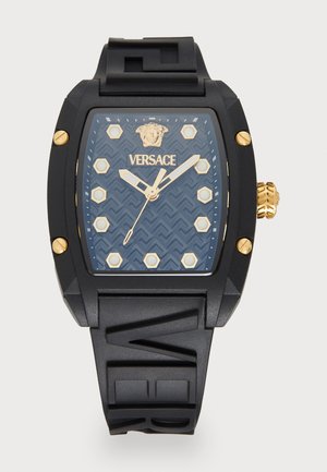Versace watch with a rectangular black silicone case, blue patterned dial, gold hour markers, and logo. Textured rubber strap with raised letters.