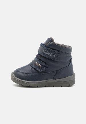 Marineblaue Kinderknöchelstiefel mit zwei Klettverschlüssen, grauem Fellfutter, profilierter Sohle und Primigi-Logo auf dem oberen Riemen und an der Seite.