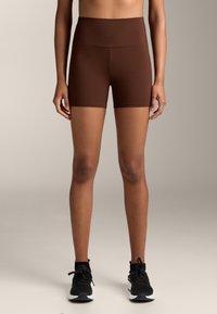 Barna, magas derekú sportnadrág sima, rugalmas anyagból, testhezálló fazonnal. Fekete edzőcipővel párosítva.