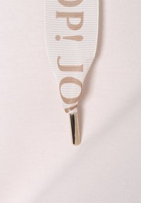 Tessuto bianco con una consistenza liscia, caratterizzato da un nastro a strisce in beige, che mostra "op" in un carattere audace, terminante con un accento metallico.