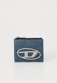 Denim piniginė su sidabriniu logo, užtrauktuko uždarymu, stačiakampio formos, tekstūruota mėlyna medžiaga ir matomais siūlų detalėmis.