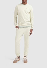 Licht beige sweatshirt met lange mouwen, ronde hals, lichte ribbels bij de mouwen, gecombineerd met bijpassende joggerbroek. Geverfde lichtbruine sneakers.