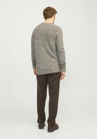 Grijze gebreide trui met een gestructureerde afwerking, ronde halslijn en lange mouwen, gecombineerd met bruine broek en donkere schoenen, bekeken van achteren.