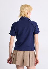 Polo bleu marine à manches courtes. Comprend un col et un design ajusté. Associé à une jupe beige plissée. Texture unie.