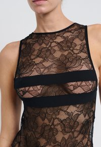 Prenda de encaje negro con patrones florales, textura translúcida con bandas negras sólidas y un diseño sin mangas.