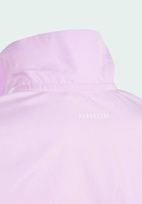 Světle růžová bunda s vysokým límcem, s hladkým, lesklým povrchem a bílým logem "AEROREADY" na zadní straně.