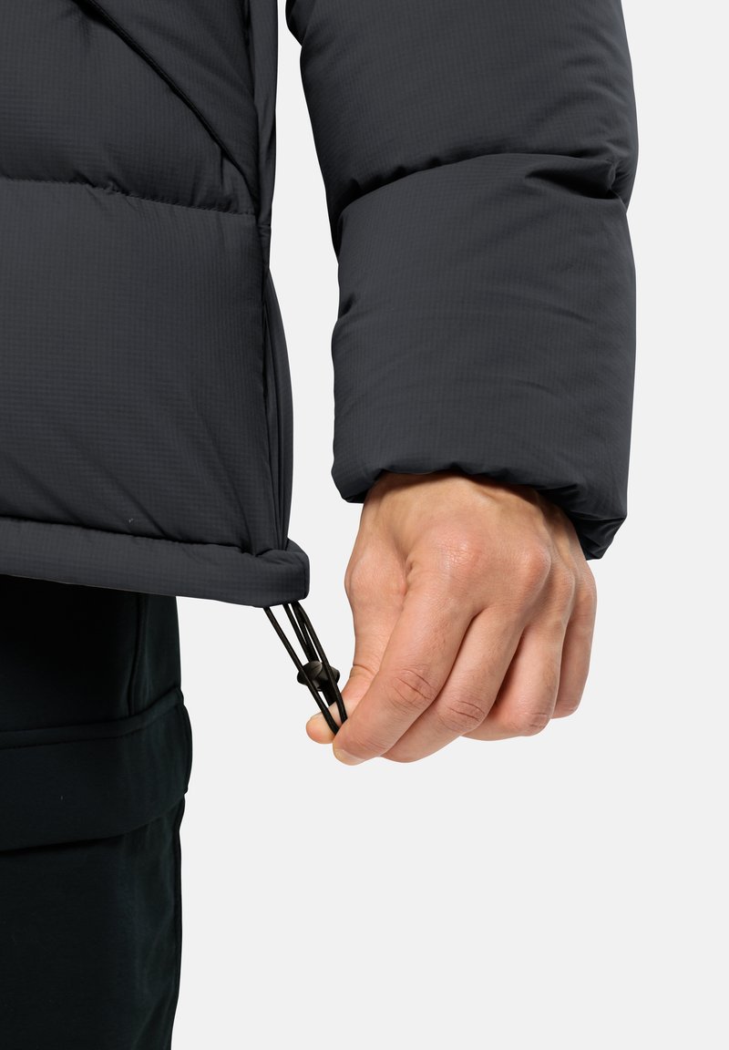 Schwarze Daunenjacke, die in der Nähe einer Hand gezeigt wird, die den elastischen Zugverschluss am Bündchen anpasst. Das Material hat eine strukturierte Oberfläche. Einfaches Design.