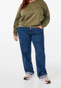 Sudadera verde oliva de manga larga, con bordados florales en los puños, combinada con jeans de mezclilla azul de pierna recta. Zapatillas ligeras.