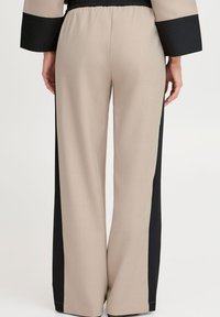 Pantalons larges beige avec des panneaux latéraux noirs, taille élastique et texture de tissu lisse. Design simple axé sur le confort et l'ajustement.