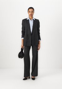 Black pinstriped suit with a double-breasted blazer, wide-leg trousers, and a light blue shirt. Accessories include a black handbag and heels.