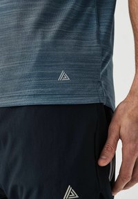 Camiseta deportiva de tela azul jaspeada, con mangas cortas, una etiqueta con un logo de triángulo y aberturas laterales para facilitar el movimiento.