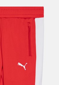 Czerwone spodnie sportowe z białą boczną lamówką, z zamkiem błyskawicznym i białym haftowanym logo. Gładka tkanina z dopasowanym krojem.