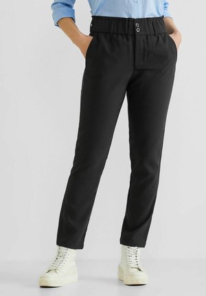 Personne portant un pantalon noir taille haute avec poches latérales, une chemise bleu clair rentrée, et des bottines blanches à plateforme lacées.