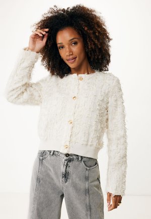 Weißer strukturierter Cardigan mit einer flauschigen Oberfläche, verziert mit goldenen Knöpfen und geripptem Saum, kombiniert mit grauen Jeans.