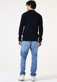 Marineblauwe geribbelde trui met lange mouwen, gecombineerd met lichtblauwe, vervaagde jeans. De outfit heeft een losse pasvorm en een eenvoudig ontwerp.