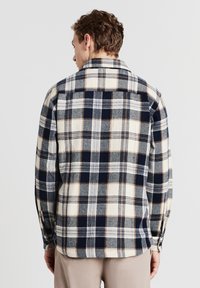 Camicia di flanella a quadri nei colori blu navy, crema e grigio. Presenta maniche lunghe, colletto e un taglio dritto con dettagli sulle cuciture laterali.