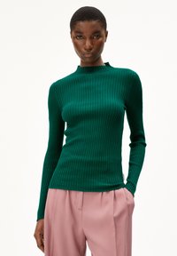 Groen geribbeld shirt met lange mouwen en een hoge nek, gecombineerd met lichtroze plissébroek. De stof vertoont een gestructureerd, slim fit ontwerp.