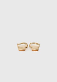 Gold flat sandals with a chain detail on the straps, featuring a smooth texture and a simple, minimalistic design.