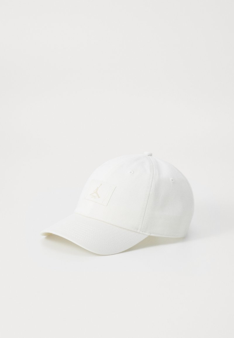 Hvid baseballkasket lavet af bomuld med en flad skygge, der har et diskret logo-patch i lys tan på forsiden og en knap på toppen.