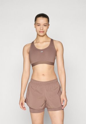 Soutien-gorge de sport marron avec bretelles réglables, associé à un short marron avec un design en couches. Les deux sont fabriqués dans un tissu lisse et léger.