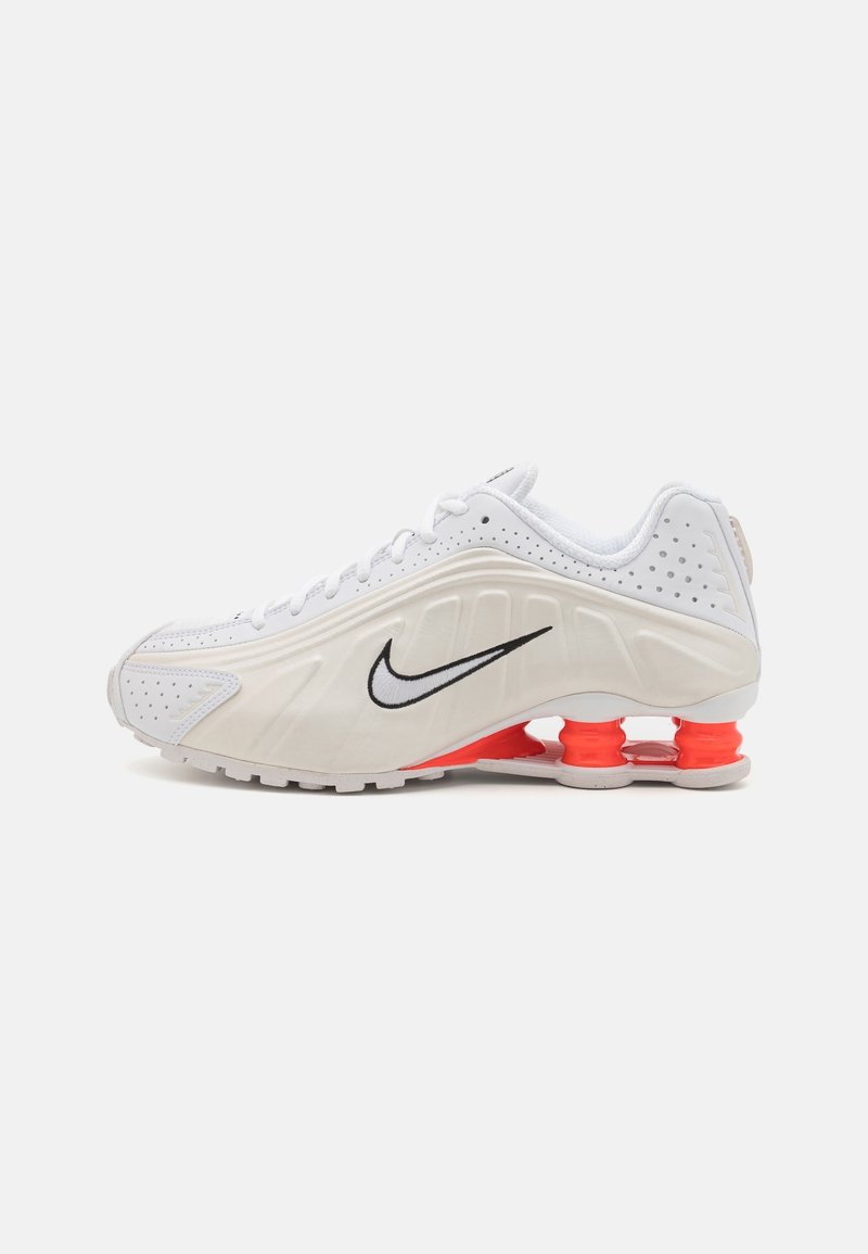Chaussure de course blanche Nike avec swoosh noir, tige perforée et amortisseurs rouges visibles dans la semelle, vue de profil.