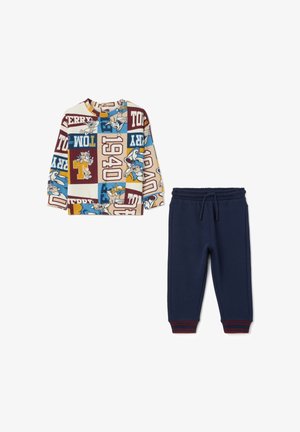 Camiseta de manga larga impresa en crema con patrones gráficos multicolores, combinada con pantalones de chándal azul marino que cuentan con una cintura elástica con cordón.