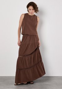 Completo marrone in due pezzi composto da un top senza maniche e una maxi gonna a strati con dettagli in pizzo. Realizzato in tessuto leggero e testurizzato.