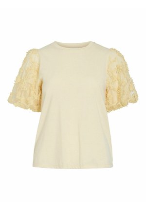 Lühike kreemjas pluus ümarate kaelusega ja läbipaistvate puhvis varrukatega, mida kaunistavad tekstuuriga lilleaplikatsioonid.