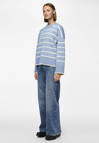 Ljusblå randig tröja med vida ärmar, som bärs tillsammans med baggy blå jeans och svarta ankelstövlar. Enkelt mönster med kontrasterande ränder.