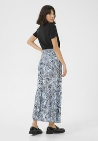 Maxi skirt with a smocked waist, featuring a blue fabric adorned with a black leaf pattern, paired with a simple black top and black shoes.