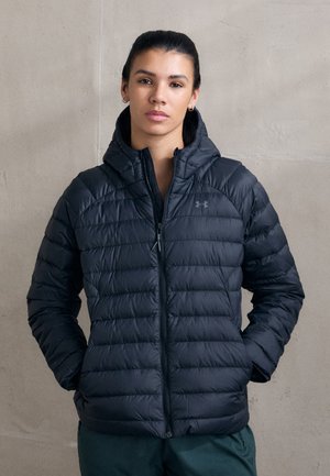 Doudoune noire avec capuche, présentant un design matelassé et une fermeture éclair à l'avant. Le matériau semble brillant et lisse. Logo Under Armour près de l'épaule.