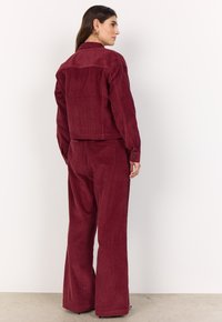 Burgundy corduroy jacket with a cropped design, paired with matching wide-leg pants. Features vertical ribbed texture and button accents.