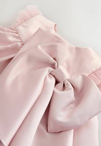 Helles pinkes Satin-Gewebe mit einer großen, strukturierten Schleife und fransigen Akzenten. Glatte Textur mit sanften Drapierungsdetails.