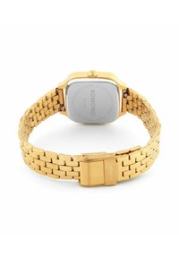 Vue arrière d'une montre-bracelet Komono ton doré avec un bracelet en métal lié et une boucle, montrant le fond en acier inoxydable et la couronne.