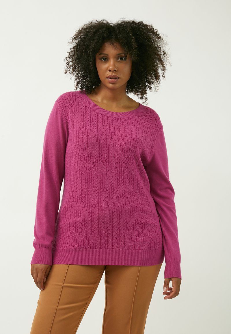 Fuchsia sweater med struktureret strikmønster, rund halsudskæring og lange ærmer. Kombineret med brune bukser for kontrast.