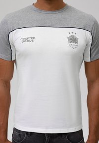 White short-sleeve t-shirt with gray shoulder accents, featuring "CRAFTED GOODS" text and a shield logo with palm trees and three stars.