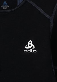 Zwarte textielshirt met ribbeltextuur, Odlo-logo in het wit en contrasterende navy-stiksel. Slim fit met een klassieke ronde hals.