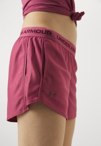 Rosa idrettsshorts laget av elastisk stoff med svart "Under Armour"-logo på midjebåndet og siden, med en avslappet passform og lommer.