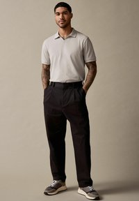 Lys grå kortærmet polo skjorte, sorte højtaljede bukser og grå sneakers med hvide snørebånd. Casual, afslappet pasform, minimalistisk design.