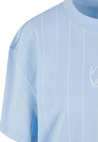Himmelblaues Baumwoll-T-Shirt mit kurzen Ärmeln, das dezente vertikale weiße Streifen und ein gesticktes Logo auf der Vorderseite aufweist.