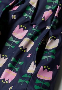 Mörkblått tyg med rosa och vita stiliserade tulpanblommor och gröna blad, som visar en närbild av en söm eller ficköppning.